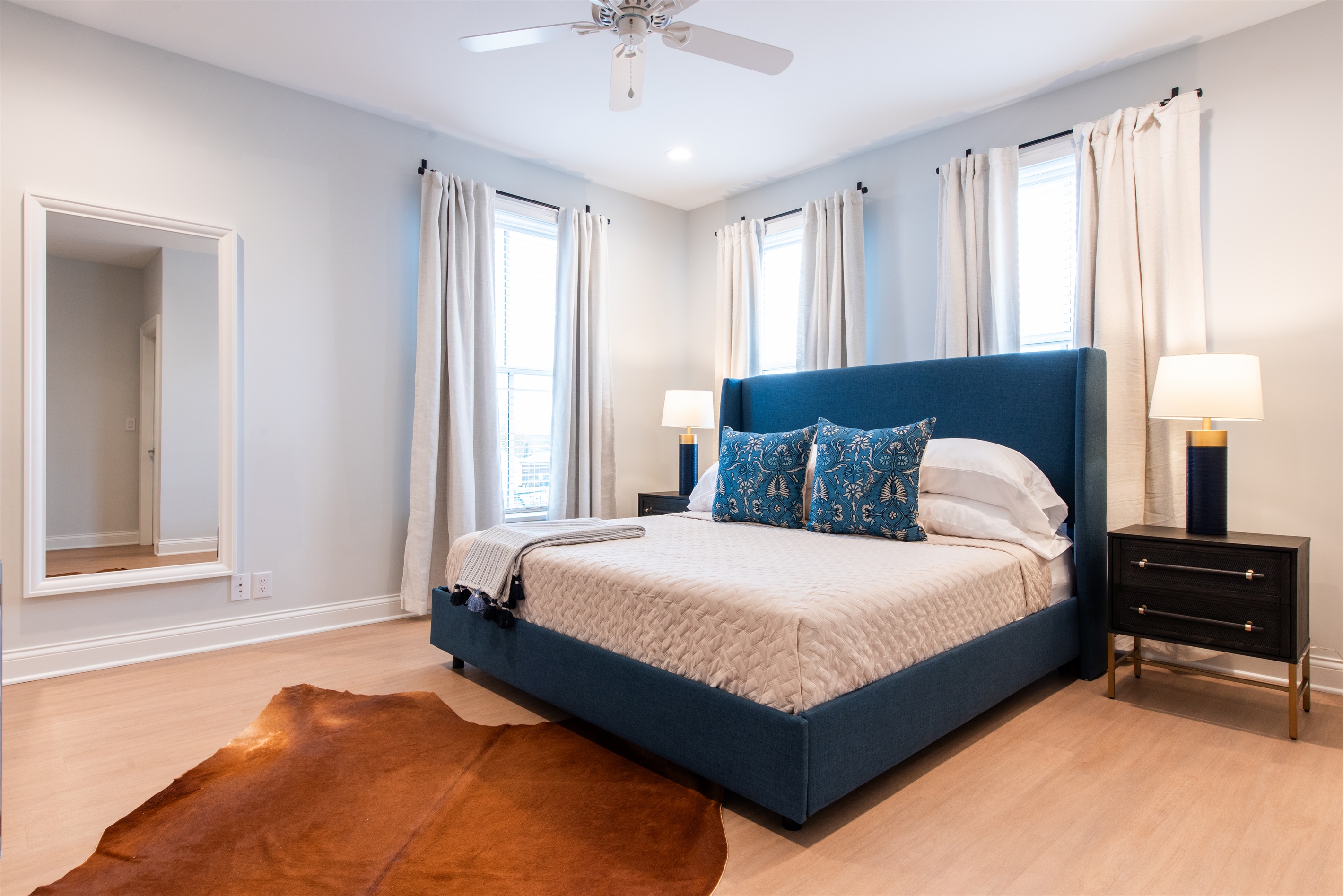 Unwind in this stylish bedroom featuring a plush blue headboard, chic decor, and natural light streaming through large windows. The cozy ambiance is perfect for your stay on the Bourbon Trail, offering both comfort and elegance.