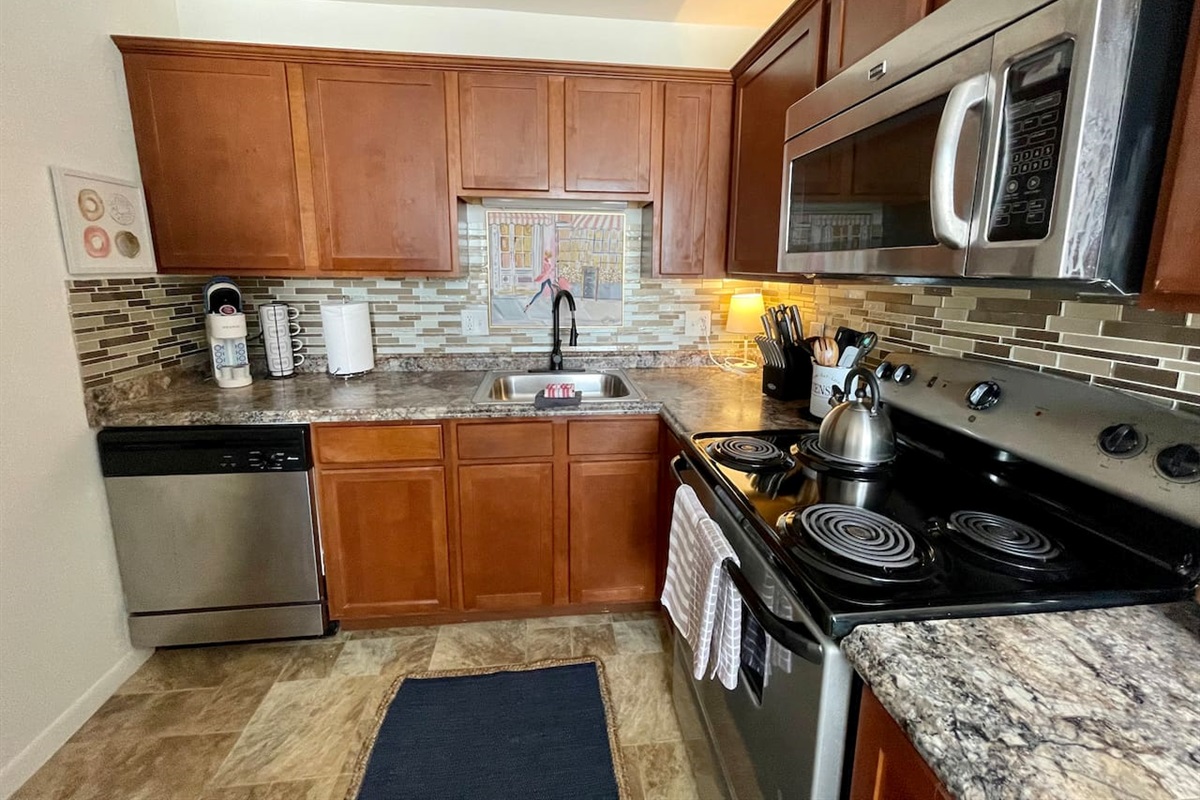 Fully equipped kitchen with stainless steel appliances, rich wood cabinetry, and stylish backsplash. Enjoy the convenience of a modern stove, microwave, dishwasher, and all the essentials needed to cook and dine comfortably during your stay.
