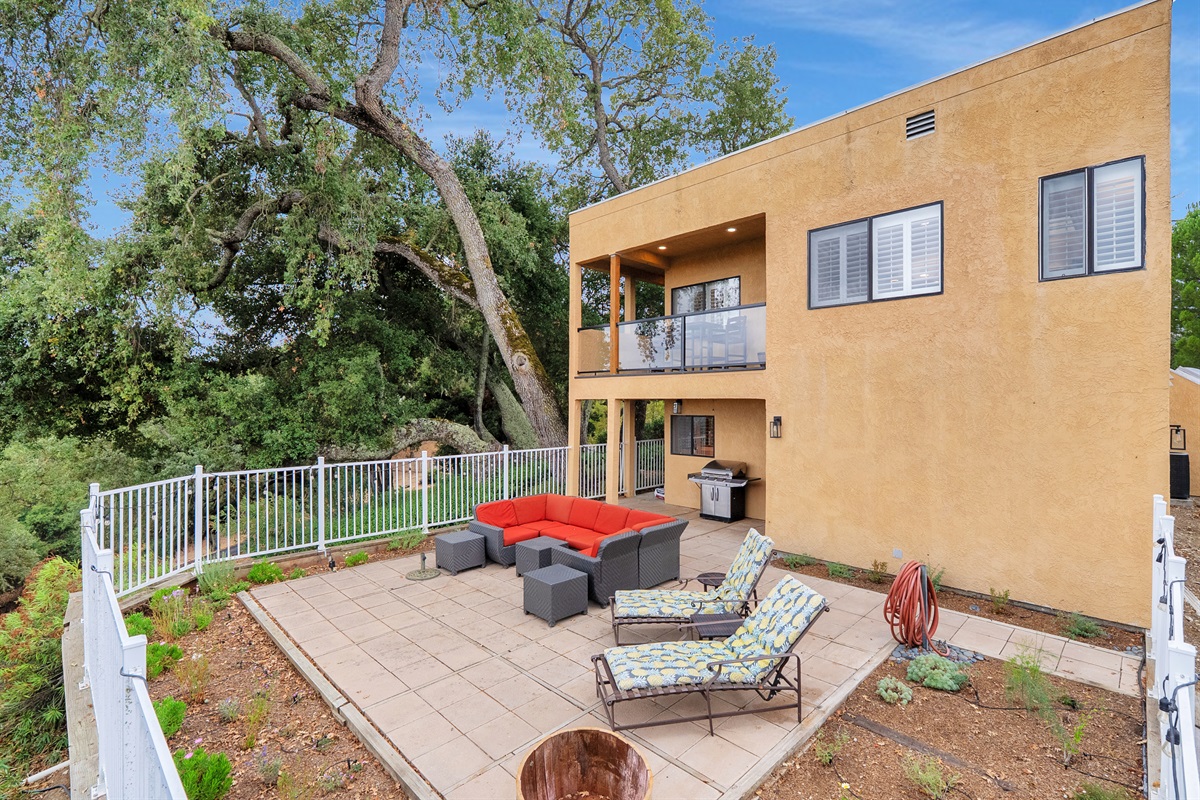 Enjoy the perfect blend of modern architecture and natural beauty. This home shows a lower patio for lounging on the vibrant sectional and grilling, complemented by an upper balcony for elevated views.