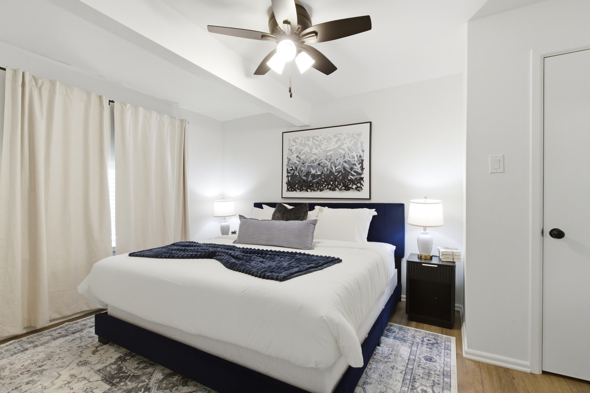 Bedroom 1 with King Bed, navy upholstered headboard, Ceiling Fan, and Smart TV. Soft Bed Linens, Extra Pillows and Blankets, and Clothing Storage for the full stay.
