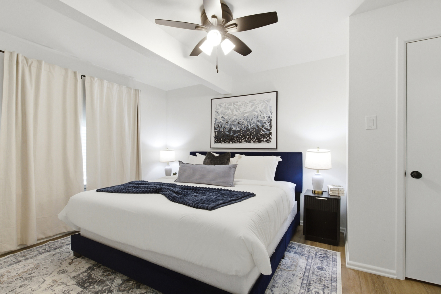 Bedroom 1 with King Bed, navy upholstered headboard, Ceiling Fan, and Smart TV. Soft Bed Linens, Extra Pillows and Blankets, and Clothing Storage for the full stay.
