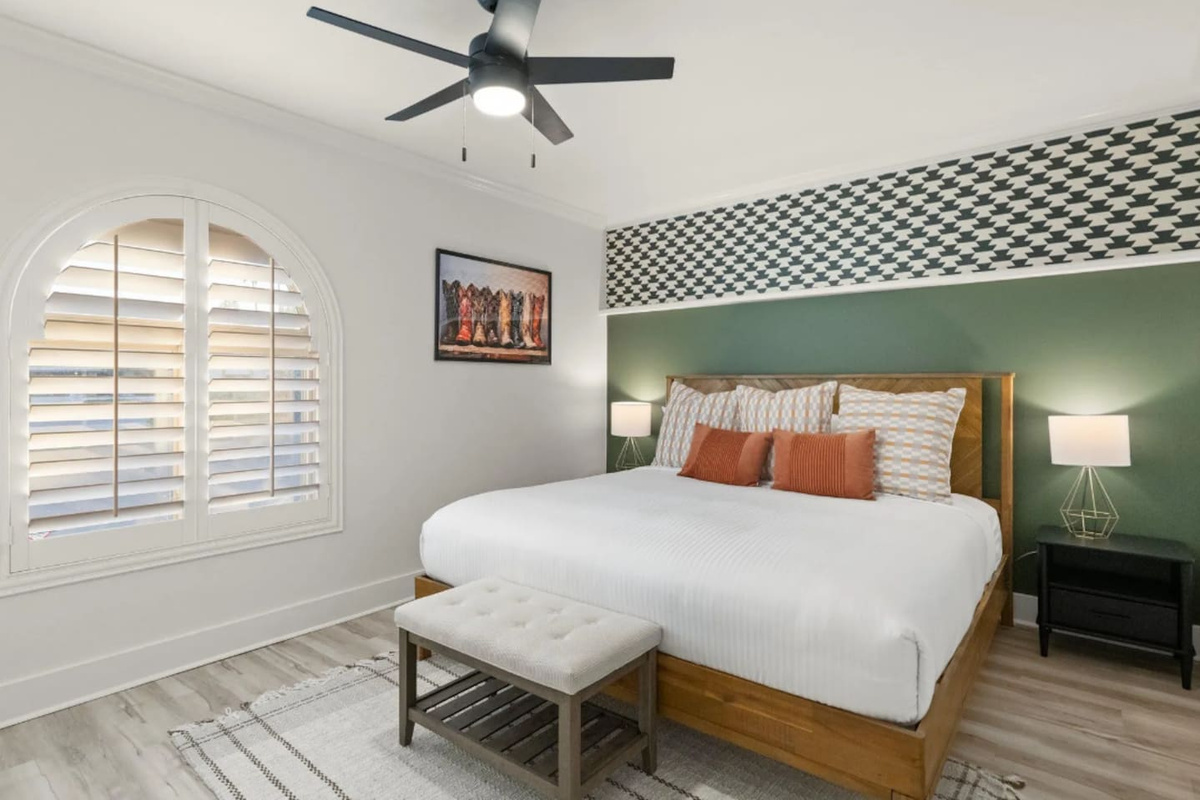A houndstooth accent and rich green wall frame the king bed, with a playful boot print nodding to the western spirit throughout the home. Arched shutter windows and warm bedside lighting round out a room that feels both cozy and stylish.