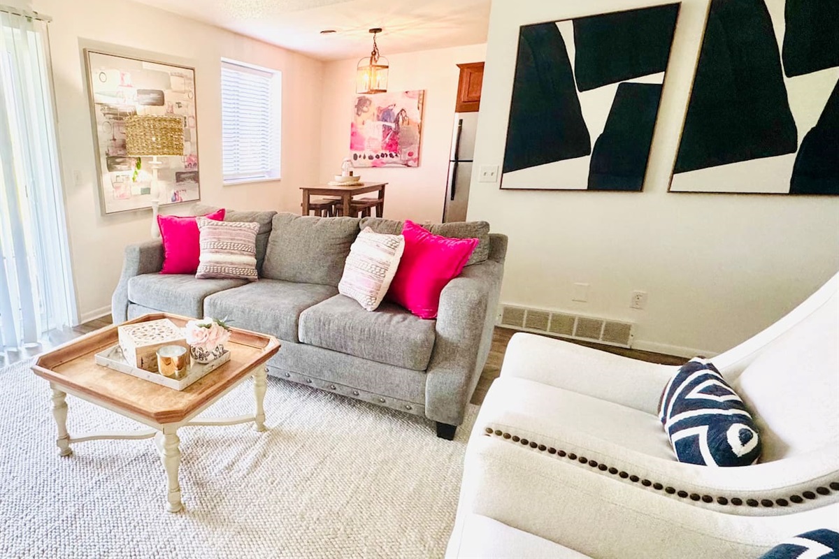 Bright and inviting living space with colorful floral decor, comfortable seating, and a playful area rug. Sliding glass doors open to scenic views, filling the room with natural light—perfect for morning coffee or evening unwinding.