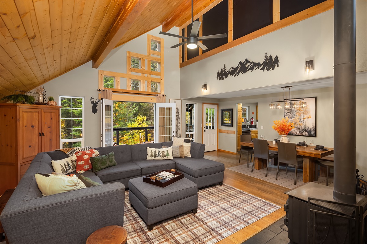 Open living room and dining room with wood burning stove and French doors out to the upper deck