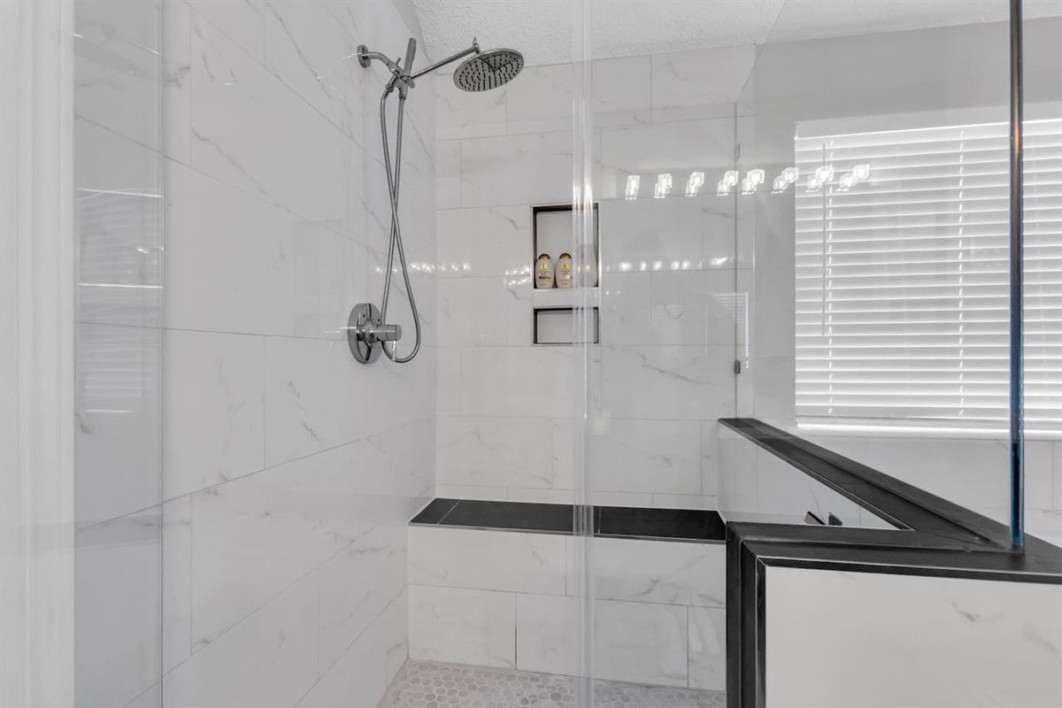 Spacious walk-in shower featuring a rain shower head, sitting space, modern finishes, fresh towels, and full bathroom essentials.