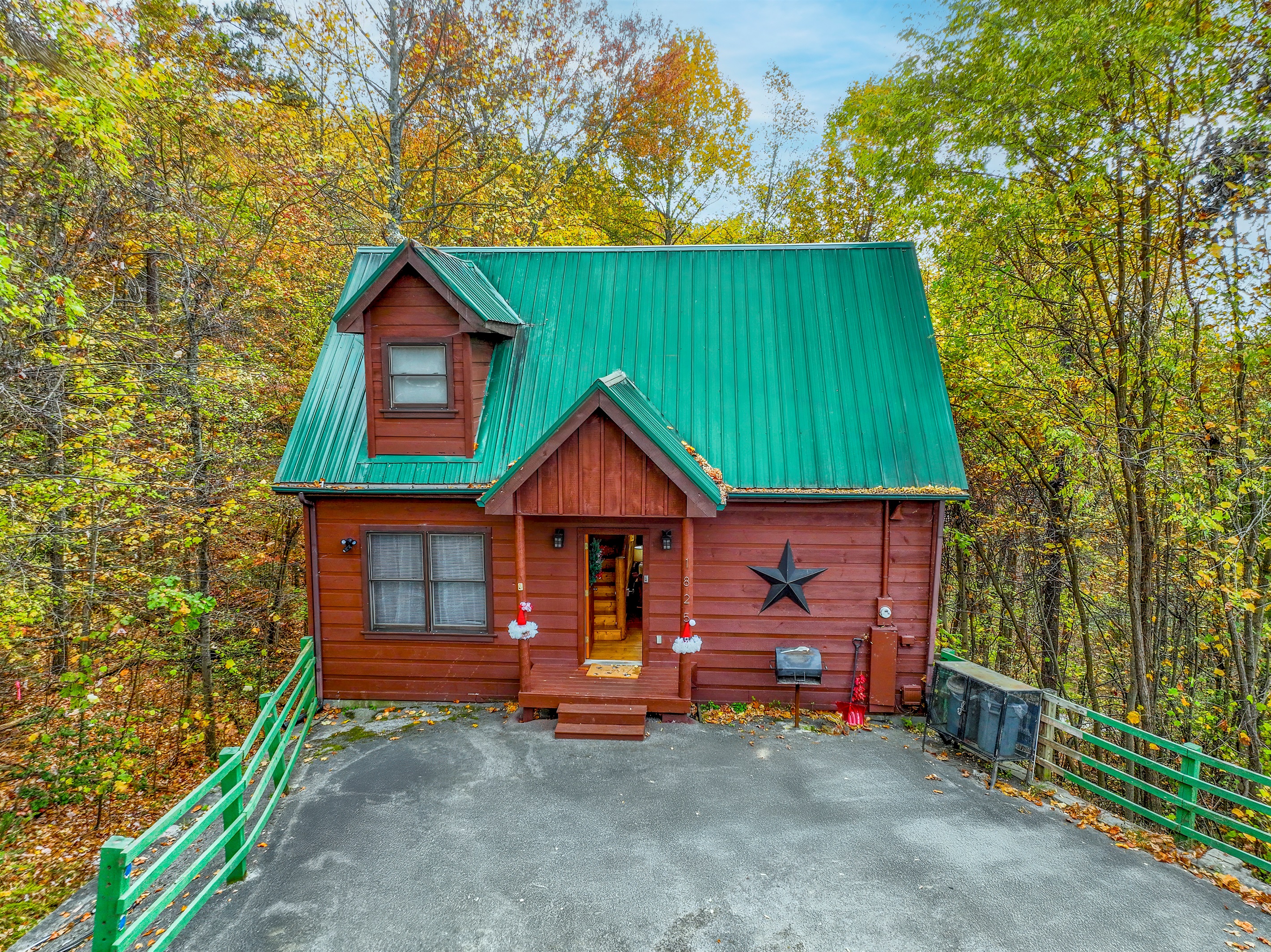 This inviting cabin showcases a green roof and warm wood tones, enhanced by soft porch lighting and a star accent, nestled among the natural beauty of the forest.