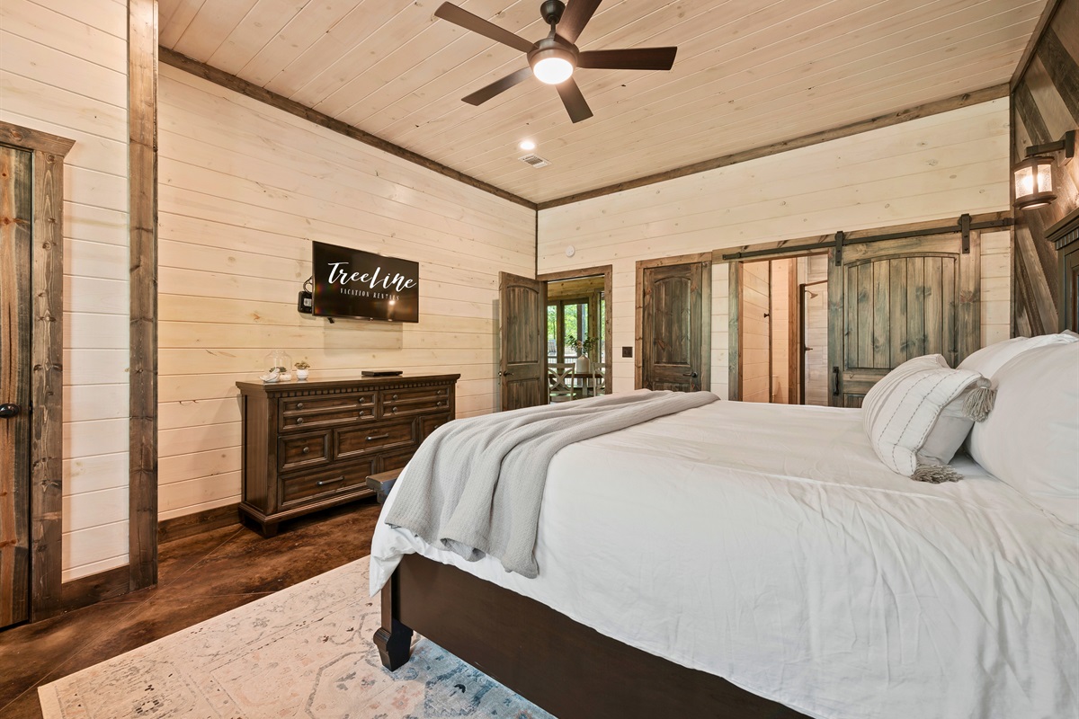 A luxurious bedroom space complete with a king-sized bed, an accent wall with wood textures, and direct access to the home's amenities.