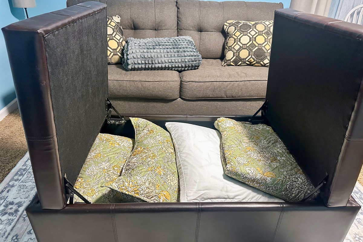 Storage ottoman in the lower-level suite containing bedding for the sleeper sofa, including linens and pillows so the space can easily convert into an additional sleeping area.