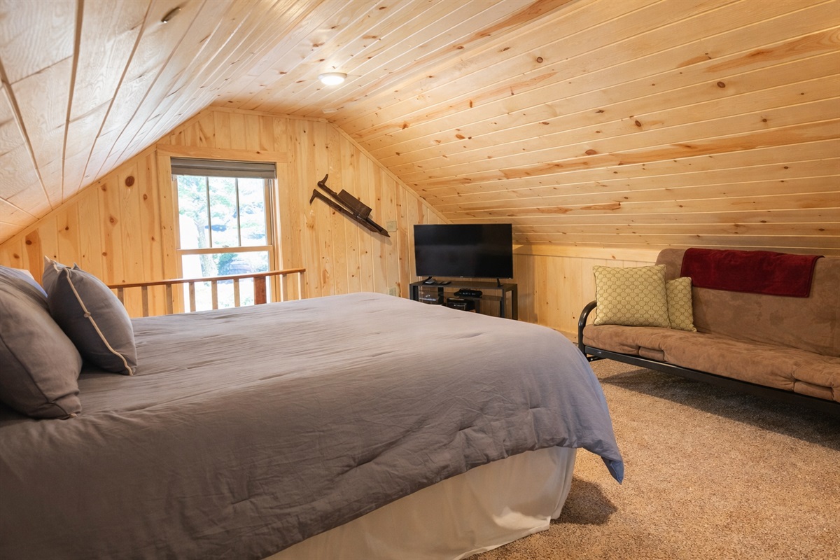 At the top of the stairs, you’re welcomed into a bright and spacious upstairs bedroom featuring a comfortable queen bed, A-frame ceilings, and a TV for winding down at night. Open to the stairway, serving as a pass-through to the second upstairs bedroom.