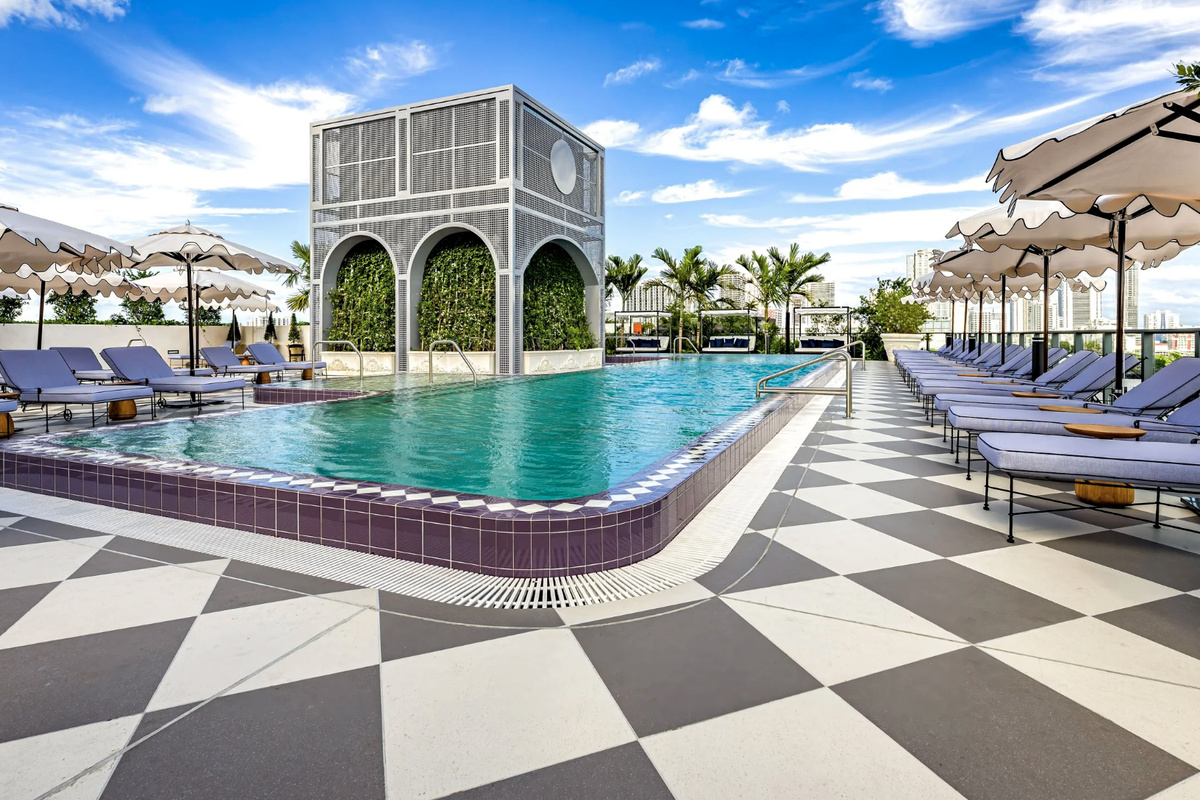 A resort-style pool framed by arched architecture, cabanas and graphic checkerboard stone - an urban oasis.