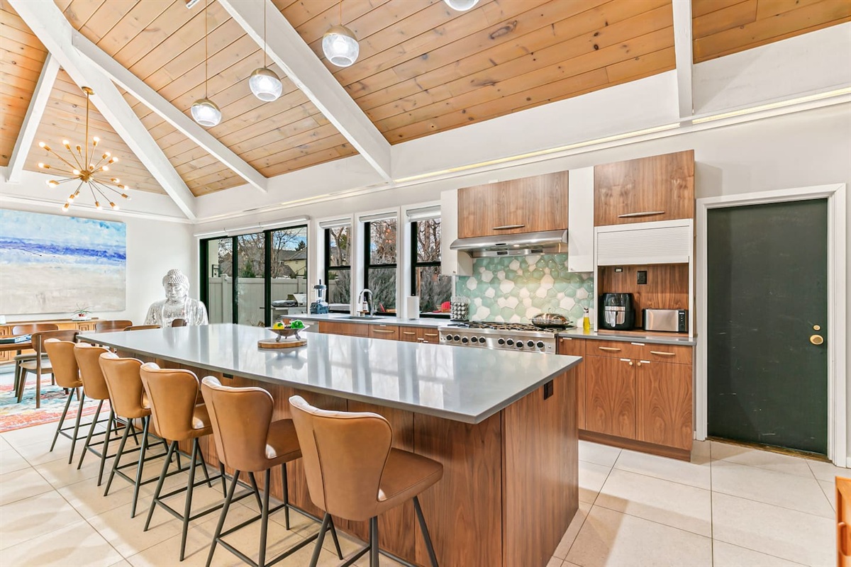 The kitchen is fully equipped with modern appliances, a Mid-Century Modern interior design, a large fridge, freezer, and ample storage. It boasts a spacious layout and a 16 ft island table, with convenient access to the outdoor area.
