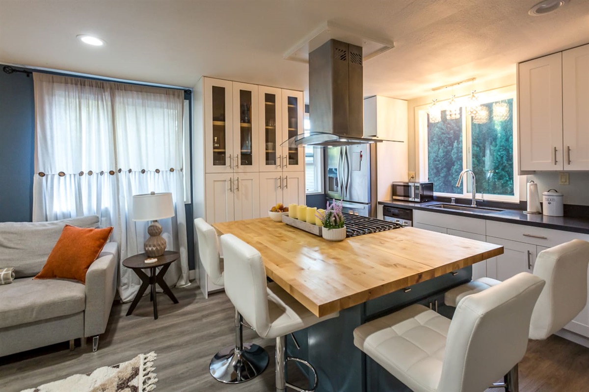 - Modern kitchen with large wood island offering seating for four guests  
- Stainless steel appliances and stylish vent hood create a sleek look  
- Open layout flows into a cozy living area filled with warm natural light