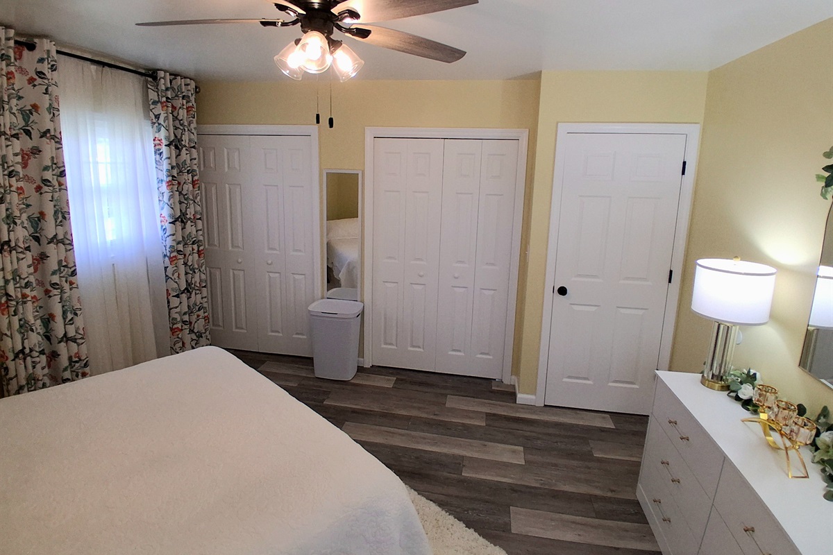 This sunny master suite feels spacious and uplifting, with soft yellow walls and floral curtains that brighten the room. Two roomy his-and-her closets offer generous storage, and natural light creates a peaceful, cheerful vibe all day.