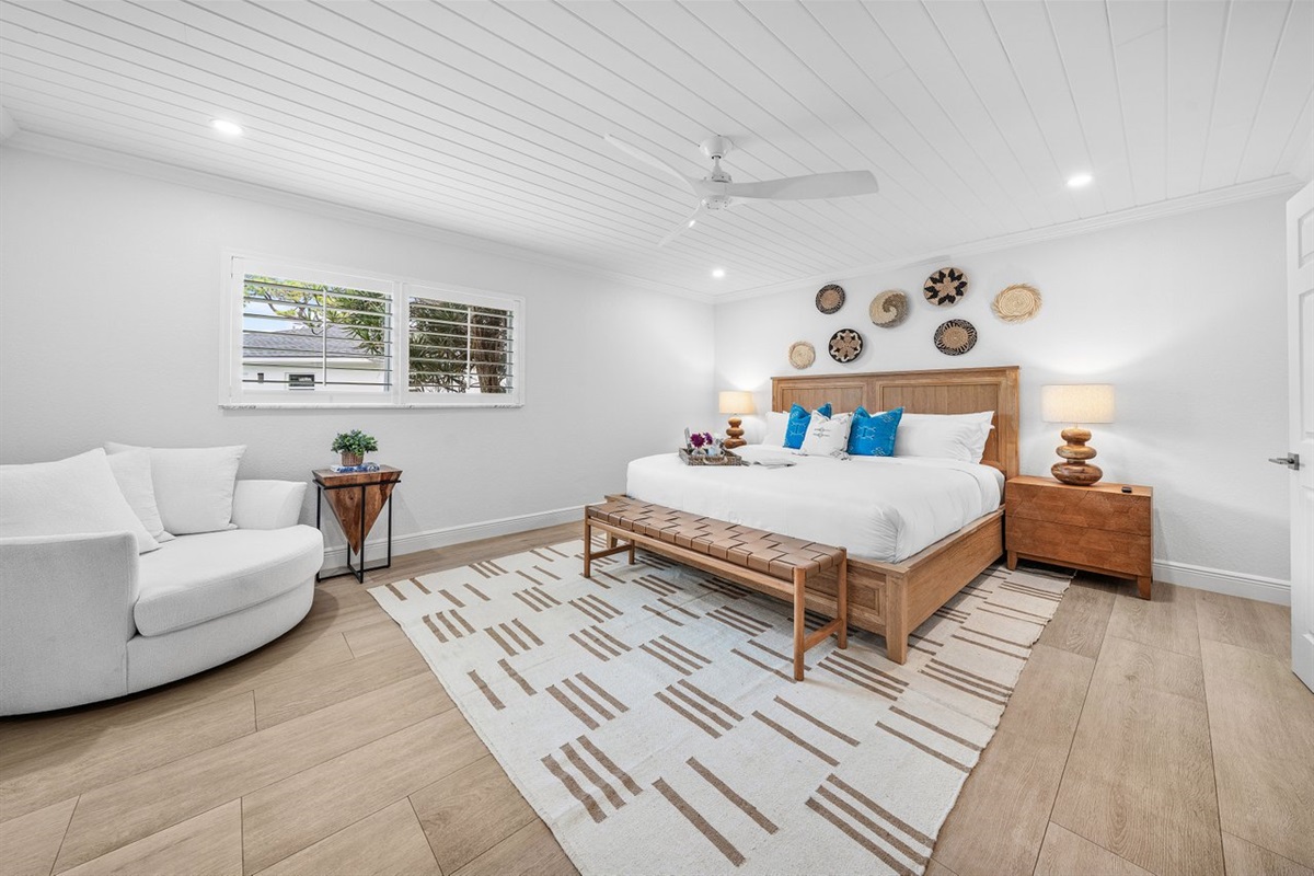 A cozy seating nook and natural light add warmth and versatility to this tranquil bedroom setting.