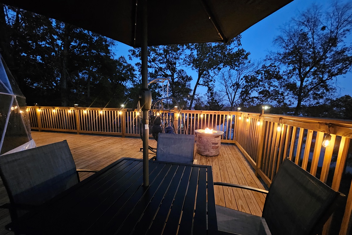 Custom-lit deck with café lighting, fire pit, and outdoor dining — perfect for quiet evenings under the trees