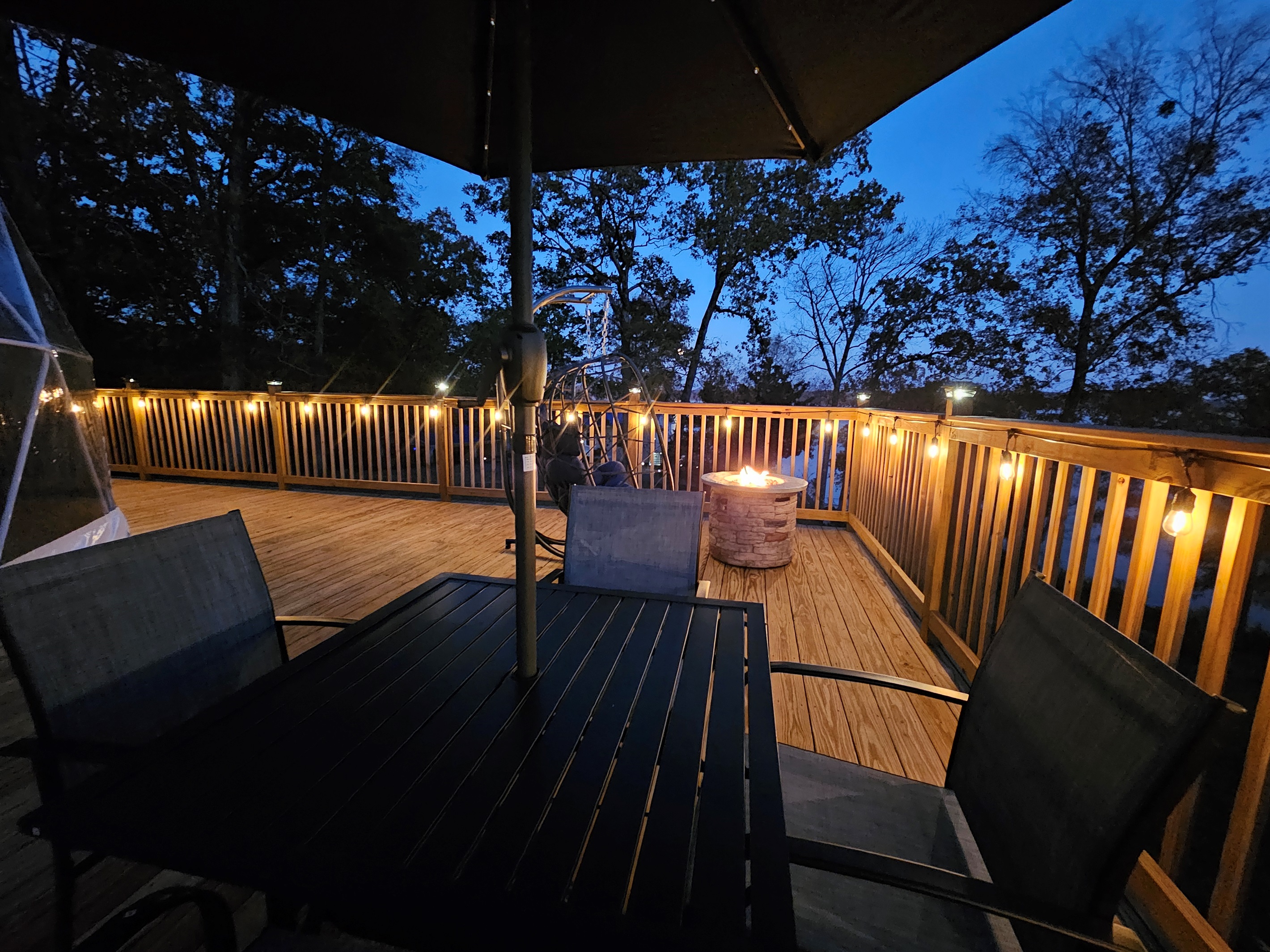 Custom-lit deck with café lighting, fire pit, and outdoor dining — perfect for quiet evenings under the trees