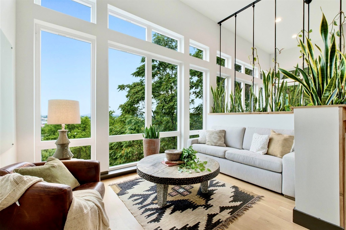 Light-soaked living area w/ floor-to-ceiling windows, white sofas & lush greenery all around.

