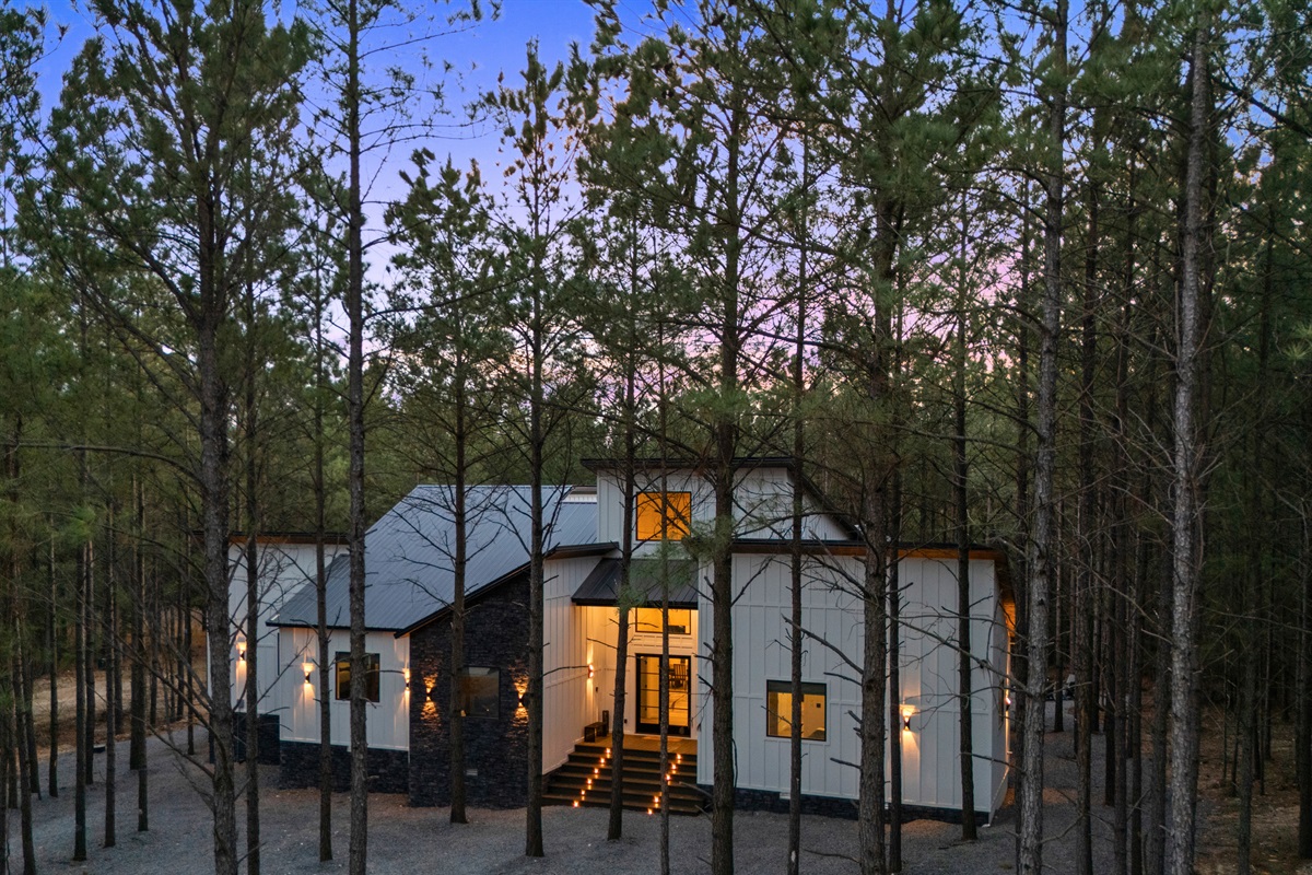 Exterior lighting highlights the modern design of the cabin while the surrounding woods create a beautiful natural backdrop.