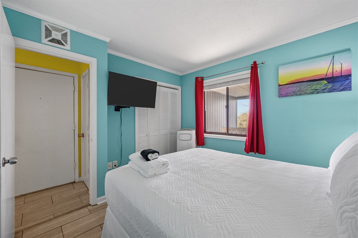 Comfortable queen bedroom with bright coastal colors, fresh linens, and a Smart TV for relaxing evenings