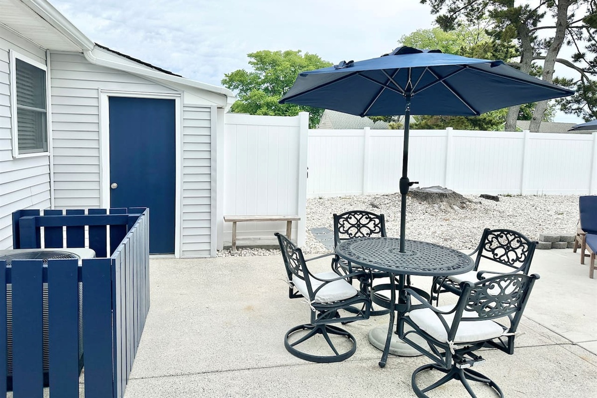 Enjoy meals at our outdoor dining set, featuring a stylish black metal table and four cushioned swivel chairs. A large navy umbrella provides plenty of shade on the spacious concrete patio, all within the privacy of a fully fenced backyard.