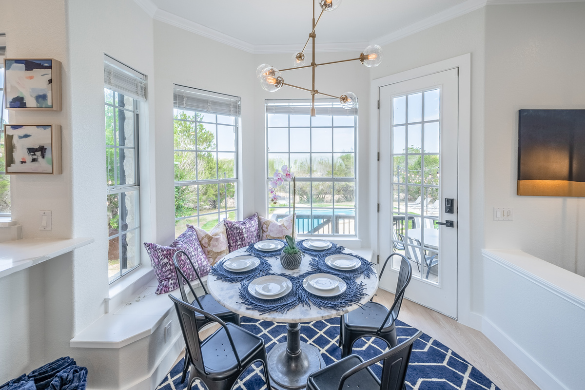 Elegant round dining table set beneath a statement chandelier, framed by garden views.