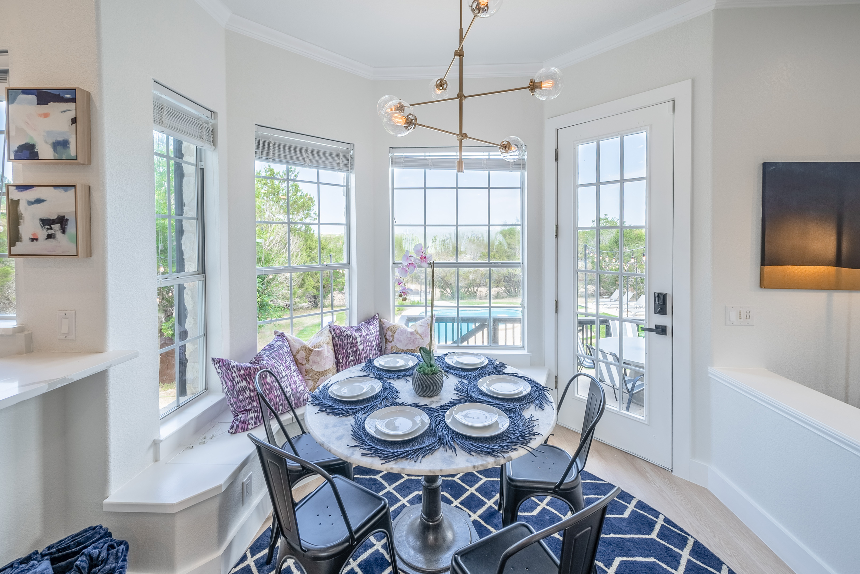 Elegant round dining table set beneath a statement chandelier, framed by garden views.