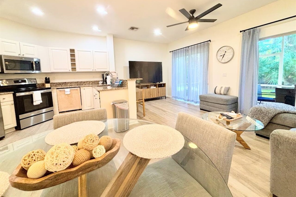 Bright modern open-concept living and dining area featuring updated finishes, comfortable seating, a fully equipped kitchen, and sliding glass doors leading to the outdoor space.
