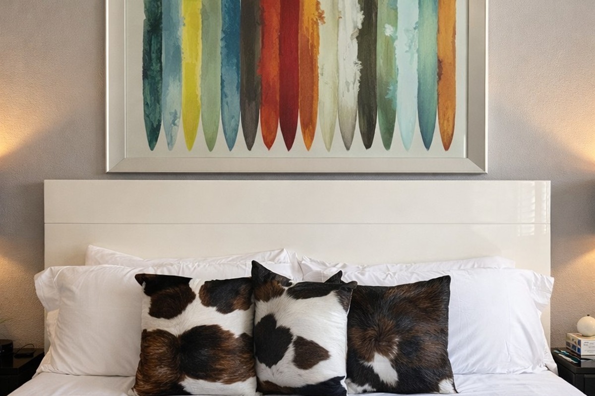 Modern bedroom with cowhide accent pillows and colorful surfboard artwork.