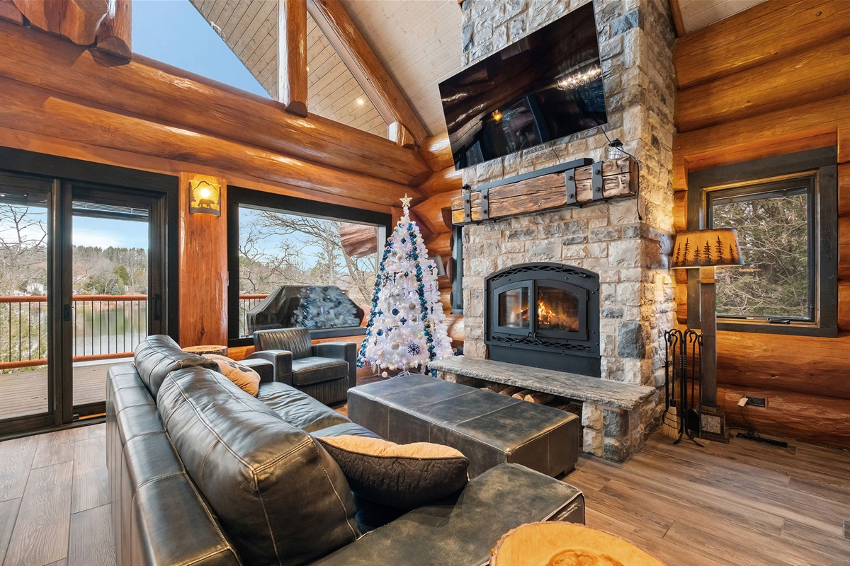 Stunning main living room featuring a grand stone fireplace, plush leather seating, and panoramic lake views—your perfect place to unwind.