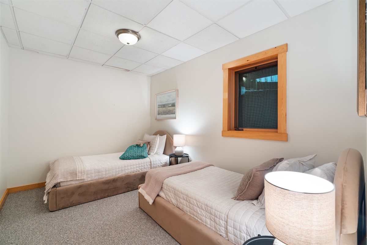 Unwind in this cozy lower-level retreat featuring plush velvet twin beds, luxe linens, a ceiling fan for comfort, and thoughtful touches like a closet and luggage racks. A full bath is just down the hall—everything you need for a restful stay. 