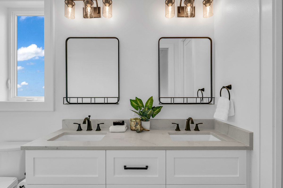 Cair Paravel: Dual vanities and sconces bring a soft glow to this ensuite, finished in classic white cabinetry.