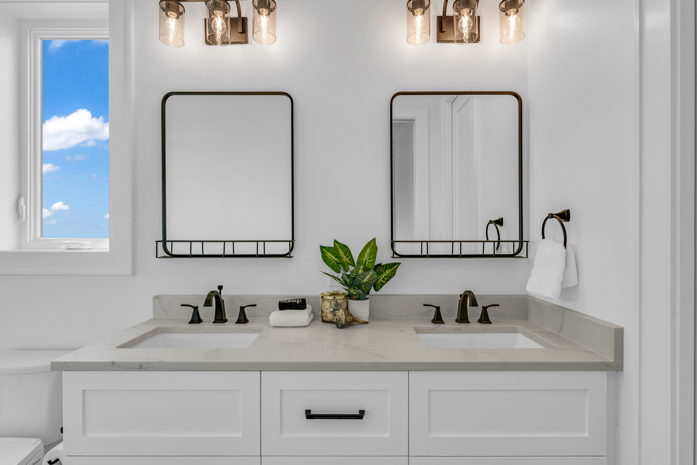 Cair Paravel: Dual vanities and sconces bring a soft glow to this ensuite, finished in classic white cabinetry.