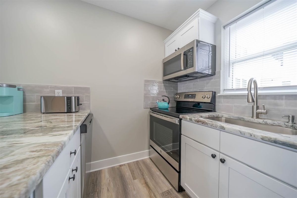 Well equipped kitchen with stainless steel range, microwave, and full size refrigerator. Quartz style counters, clean finishes, and natural light create a functional space for cooking, prepping meals, and starting the day comfortably.