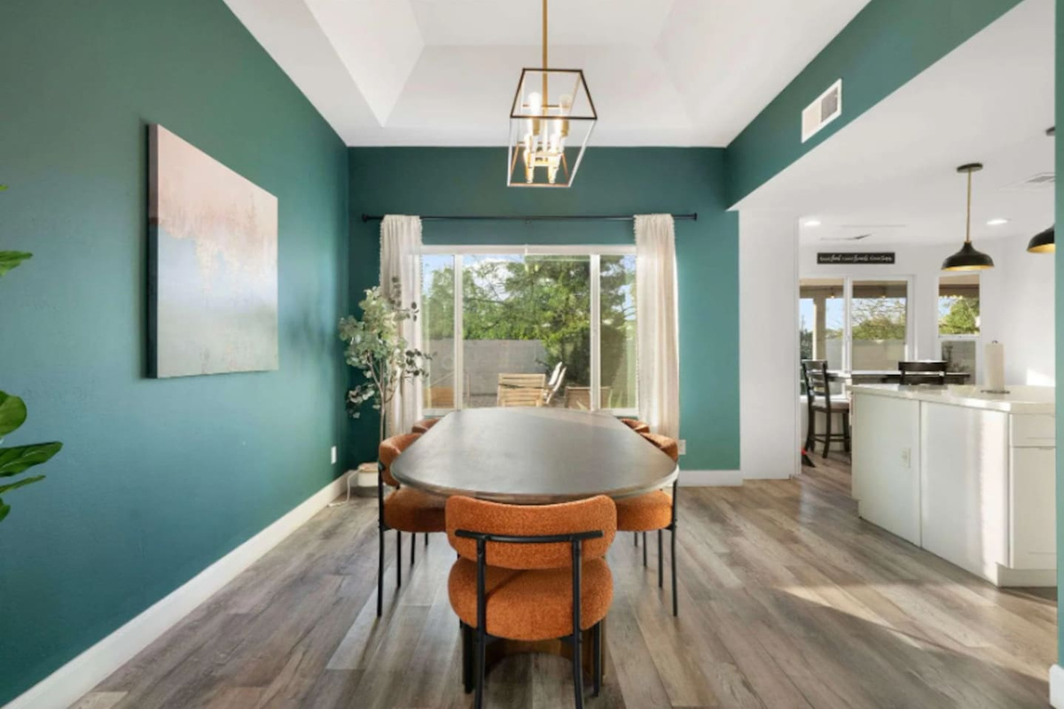 Sophisticated dining room with teal accent walls, round table, and views of backyard oasis. 