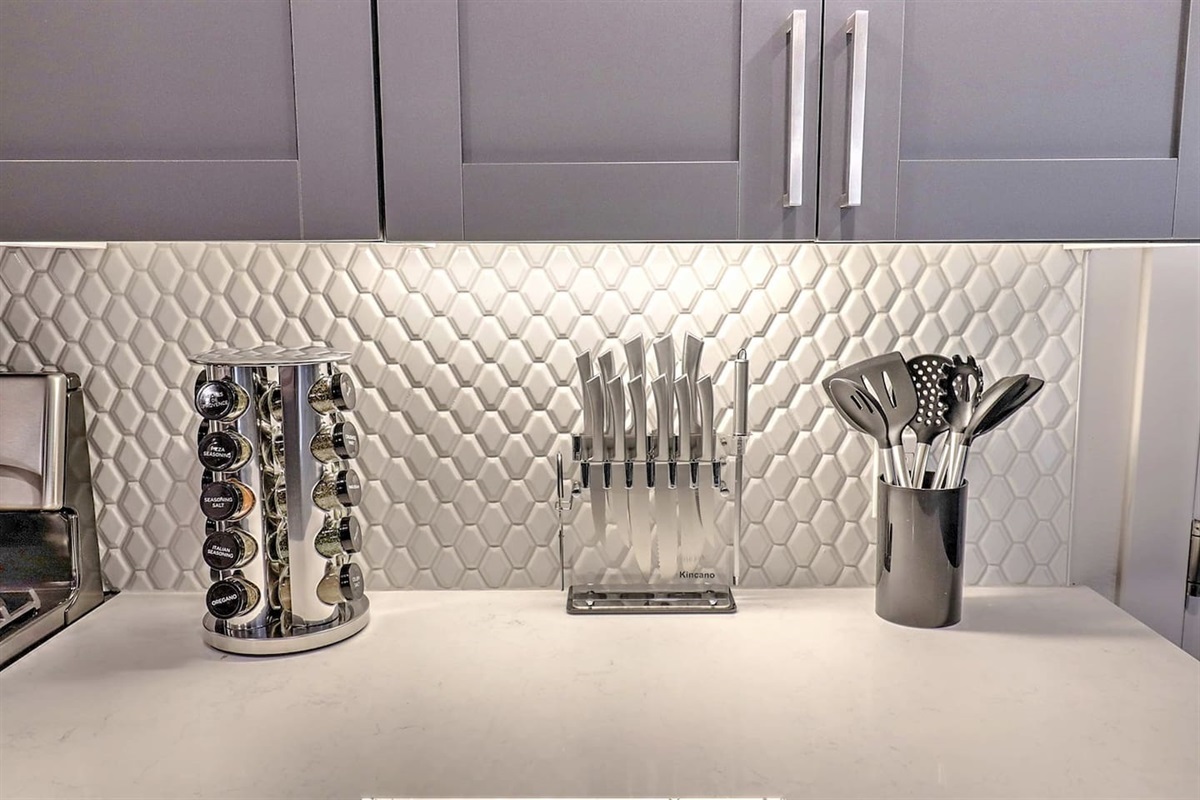 - Fully stocked kitchen setup featuring stainless utensils and sharp knife set   - Spice rack adds flavor variety for easy cooking and meal preparation   - Bright backsplash and sleek counters create a stylish cooking environment