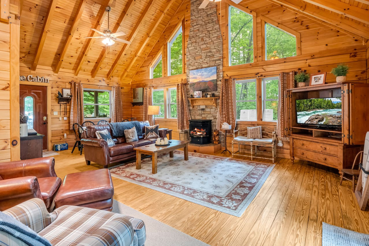 Main living room featuring high vaulted ceilings, stone fireplace and mantel, leather seating, and a television set