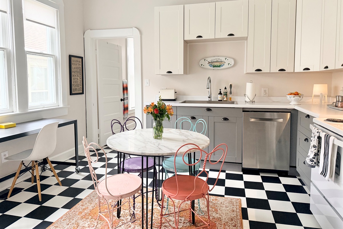 Sun-filled classic eat-in kitchen with iconic black-and-white checkerboard floors, marble café table, and a dedicated workspace for remote stays. 
