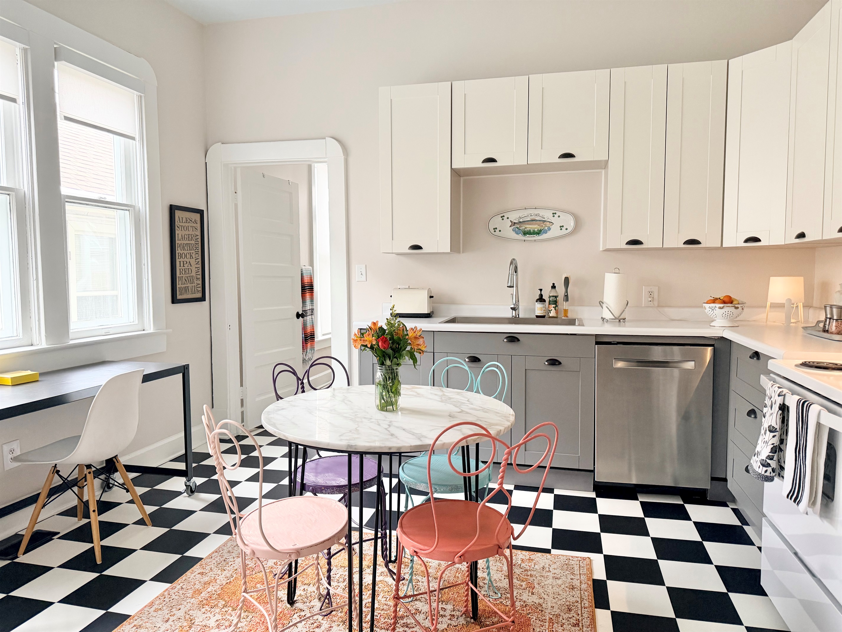 Sun-filled classic eat-in kitchen with iconic black-and-white checkerboard floors, marble café table, and a dedicated workspace for remote stays. 