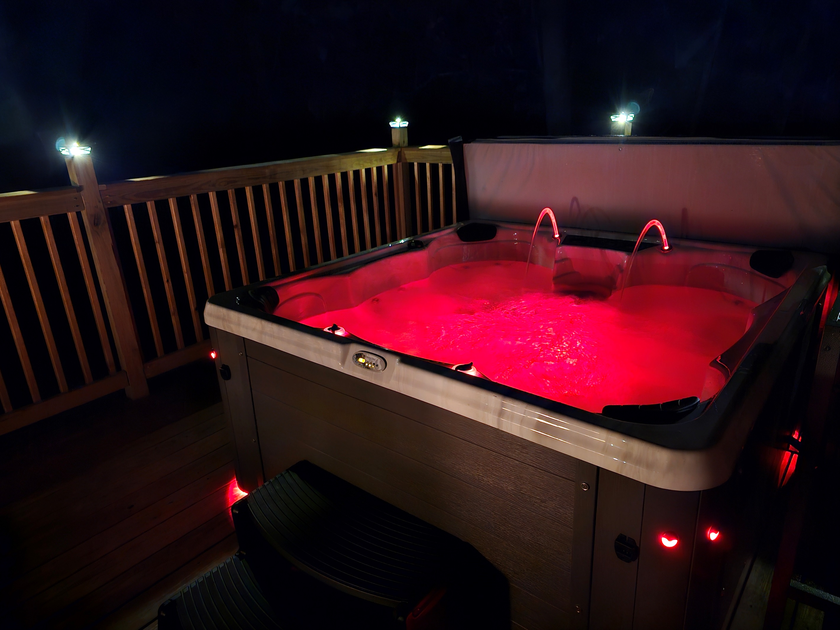 Hot tub illuminated at night with LED lighting and deck railing lights.