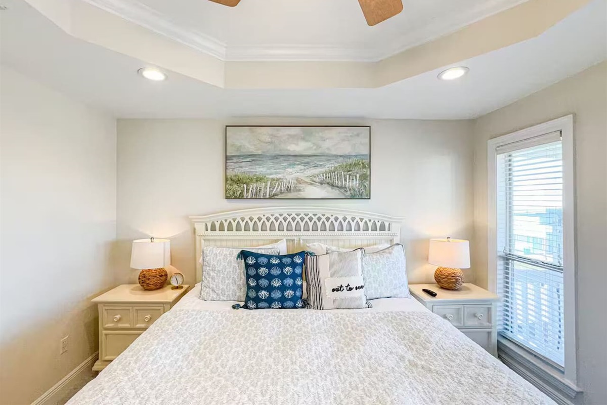 Serene bedroom with a comfortable queen bed, soft coastal decor, and plenty of natural light. Features bedside lamps, ceiling fan, and a peaceful atmosphere for restful nights.