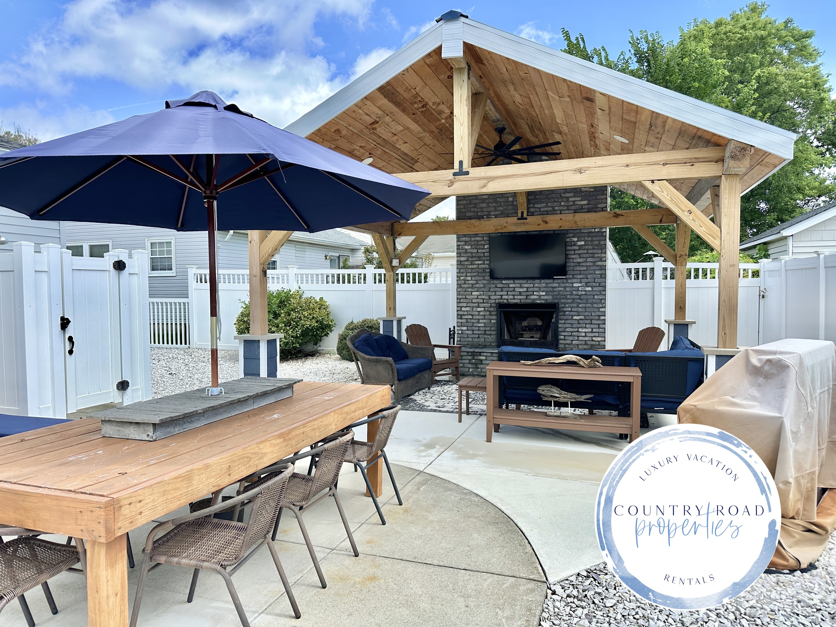 Savor alfresco meals at the spacious wooden dining table in your private backyard. This inviting space connects to a luxury covered lounge with a stone fireplace and TV, creating the ultimate setting for vacation entertaining.