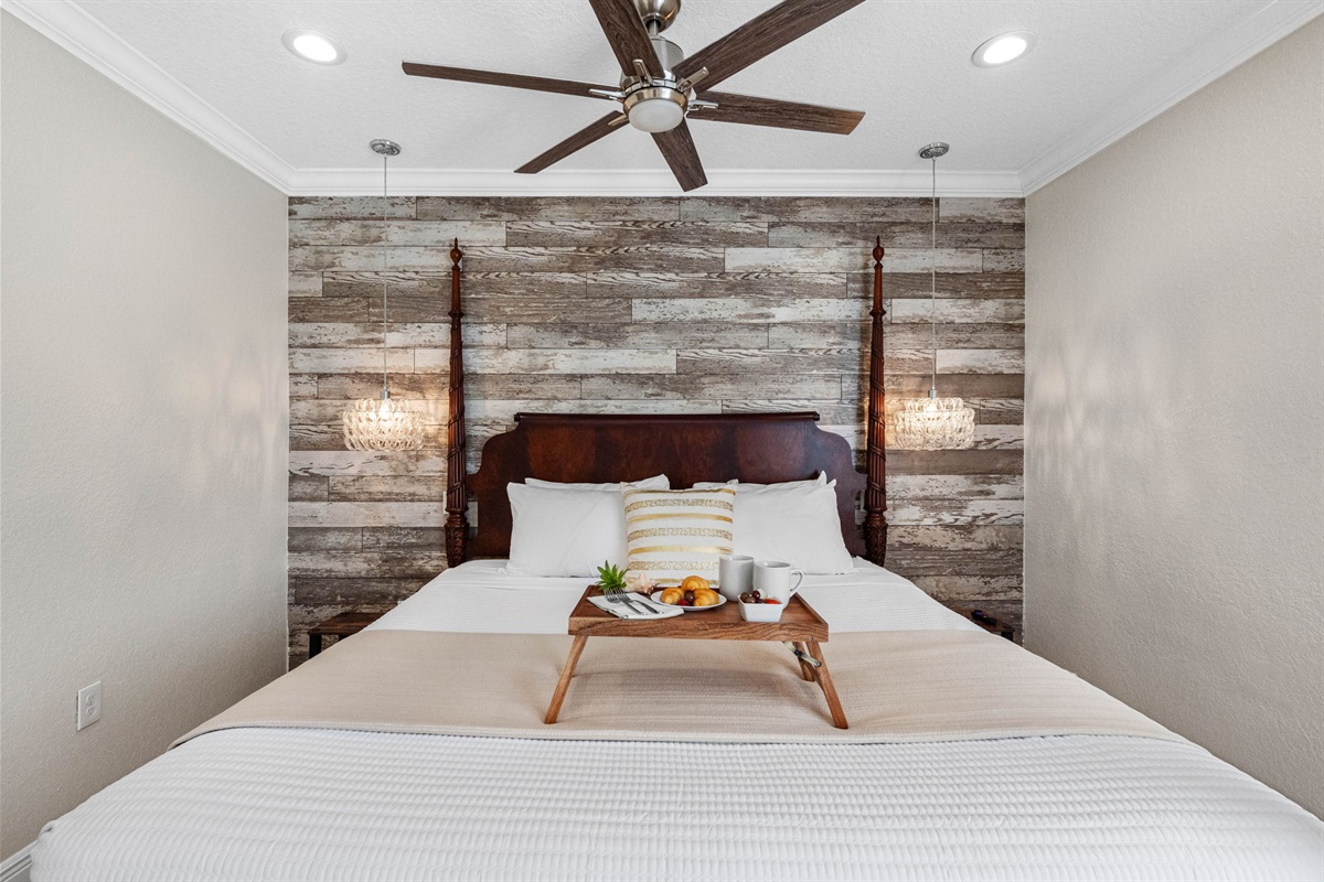 The wood-paneled accent wall and rich four-poster bed bring warmth and character, complemented by neutral tones and polished tile floors.