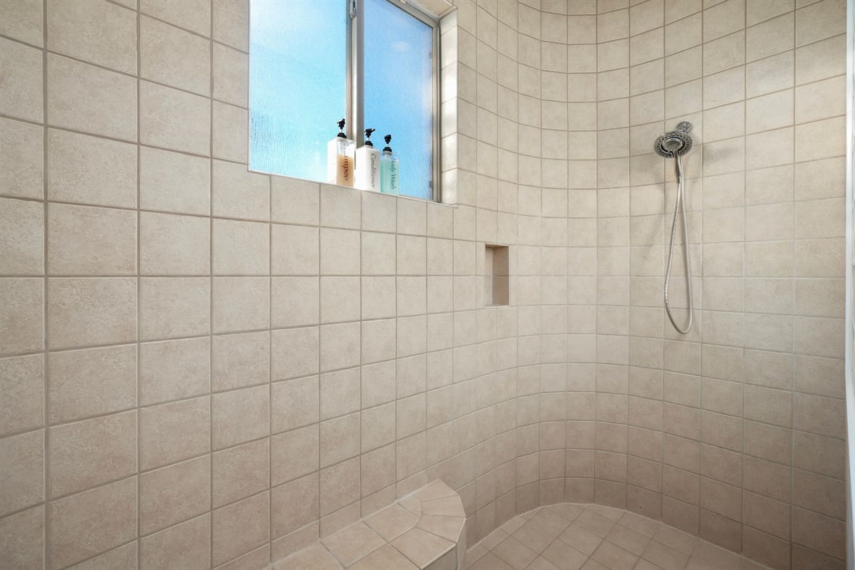Large walk-in shower with tiled walls and built-in bench seating.