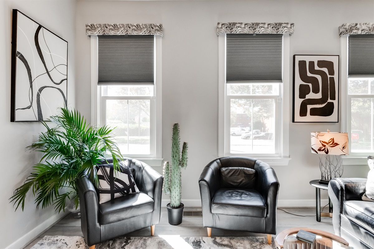 Living Room Oasis: Stylish black leather seats, vibrant decor, and sunlit windows invite relaxation!