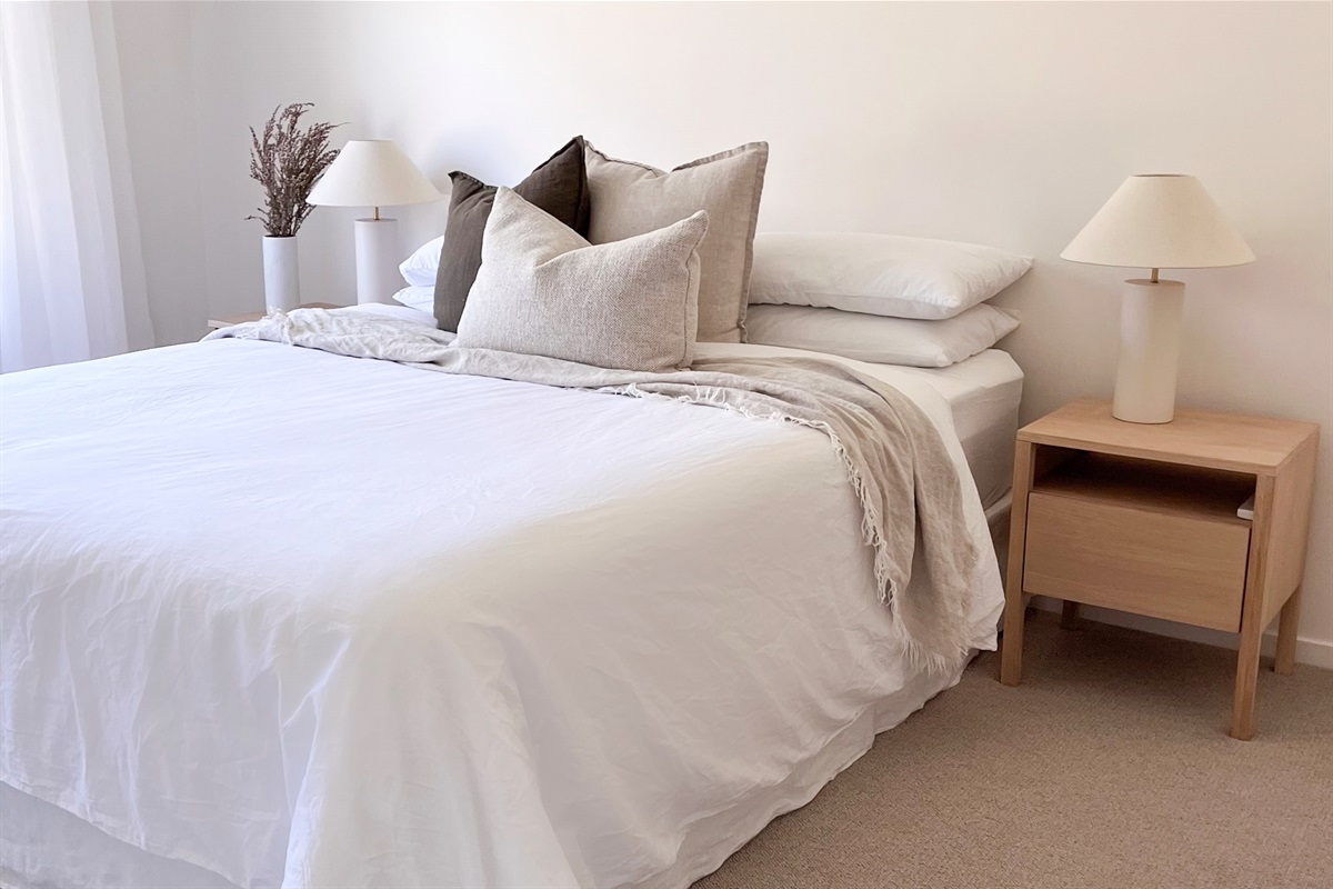 The main bedroom has a queen bed, layered pillows, bedside tables and warm lamps, with simple storage space nearby.