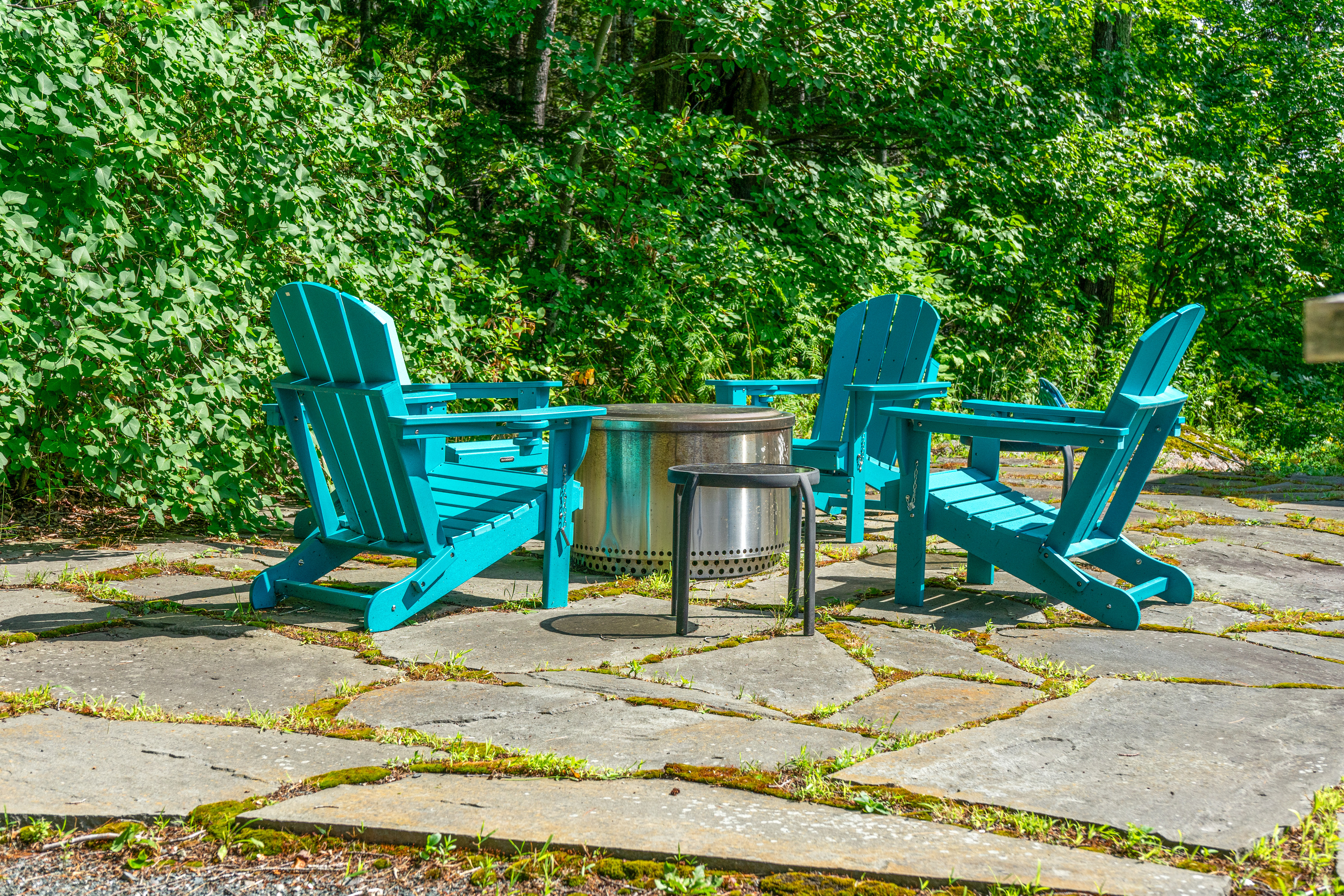 Evening campfire gatherings at "The Crag." Gather around the stainless steel smokeless fire pit in bright turquoise Adirondack chairs on the natural flagstone patio—surrounded by lush greenery on the edge of Acadia National Park.
