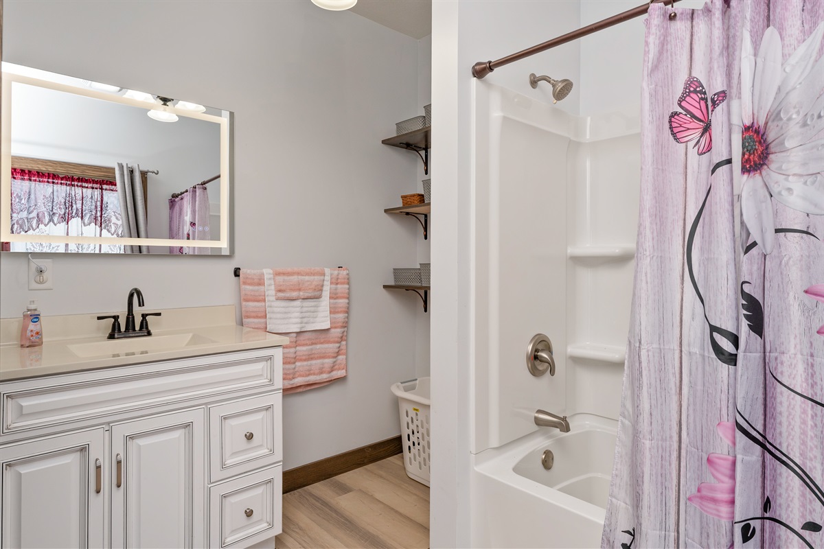Crisp white vanity, illuminated mirror, and a spacious tub/shower combo create a clean and modern upstairs bathroom with plenty of storage.