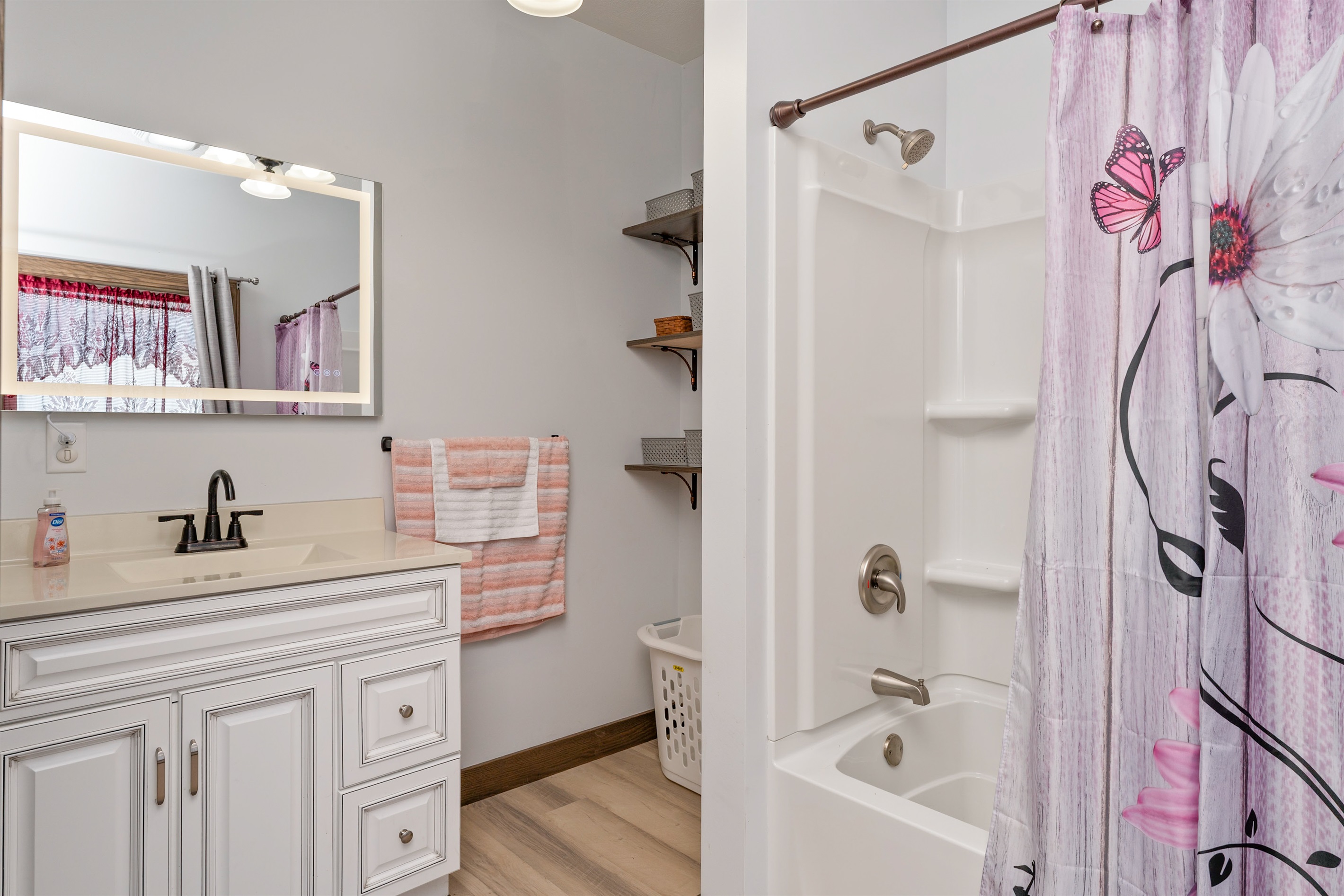 Crisp white vanity, illuminated mirror, and a spacious tub/shower combo create a clean and modern upstairs bathroom with plenty of storage.