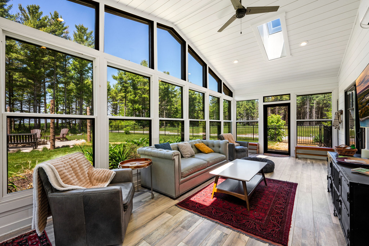 Soak up natural light in the sunroom's inviting seating area, where wraparound windows bring the outdoors in from every angle.