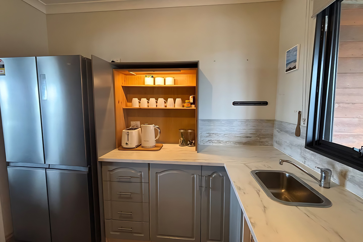 The scullery behind the kitchen's barn door holds the fridge, a second sink and a lit coffee station with a kettle, toaster and mugs, keeping everyday prep out of the main kitchen.